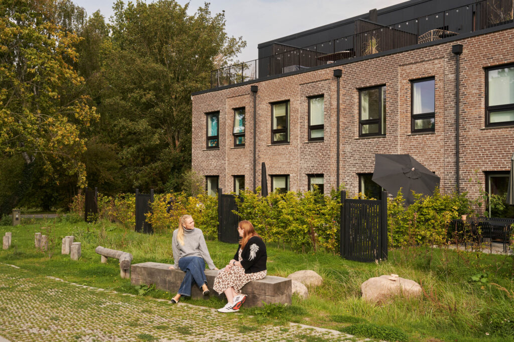 to personer snakker pÃ¥ en bÃ¦nk i biodiverst miljÃ¸ foran plantagerÃ¦kkerne